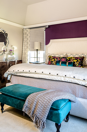 White upholstered bed with purple wallpaper, aqua bench at foot of bed and silver wall mirror