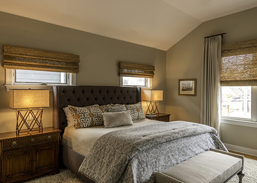 Main bedroom with taupe and grey palette, upholstered headboard and woven shades