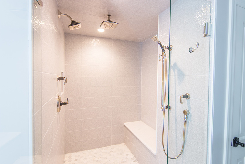 Large walk in shower with bench, white tile, glass door and multiple shower heads
