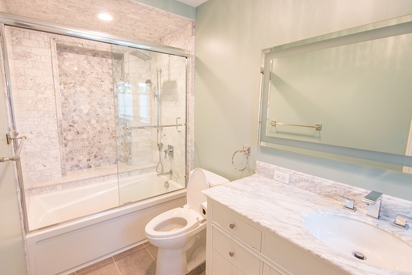 Guest bath with white vanity, tub with sliding glass doors and silver frame mirror