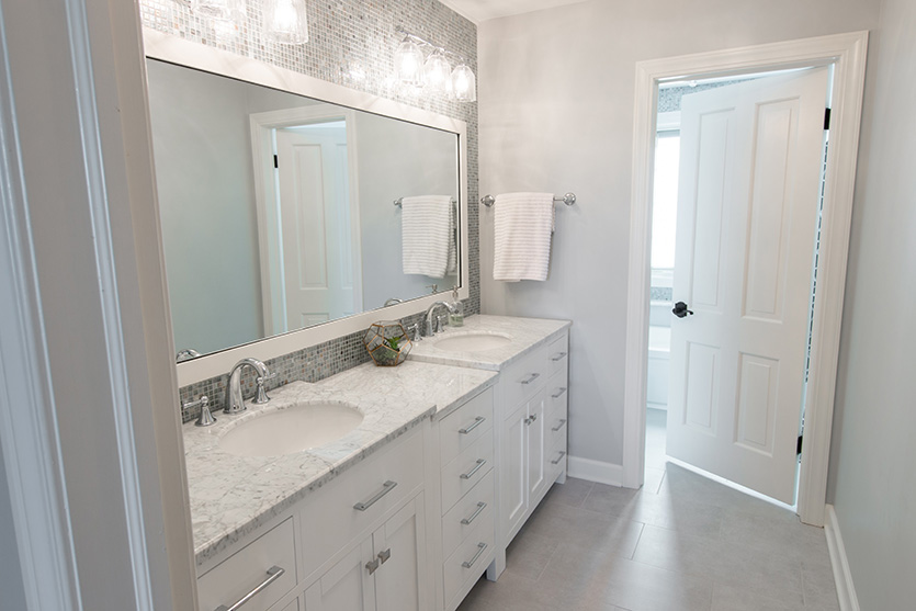 White cabinet bathroom with two sinks, large silver frame mirror and water closet