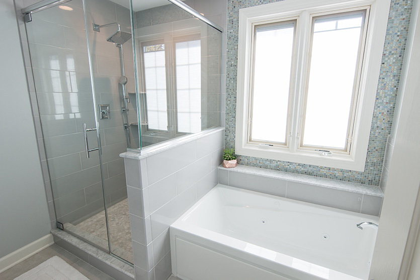 Guest bath with walk in glass shower and deep tub under windows