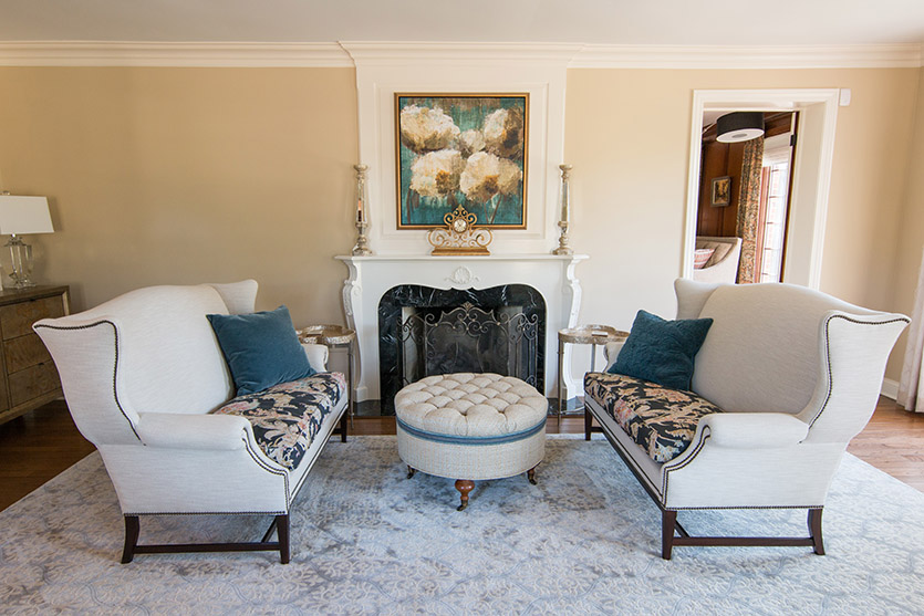 Pair of white sofas with navy floral cushions in front of formal white fireplace