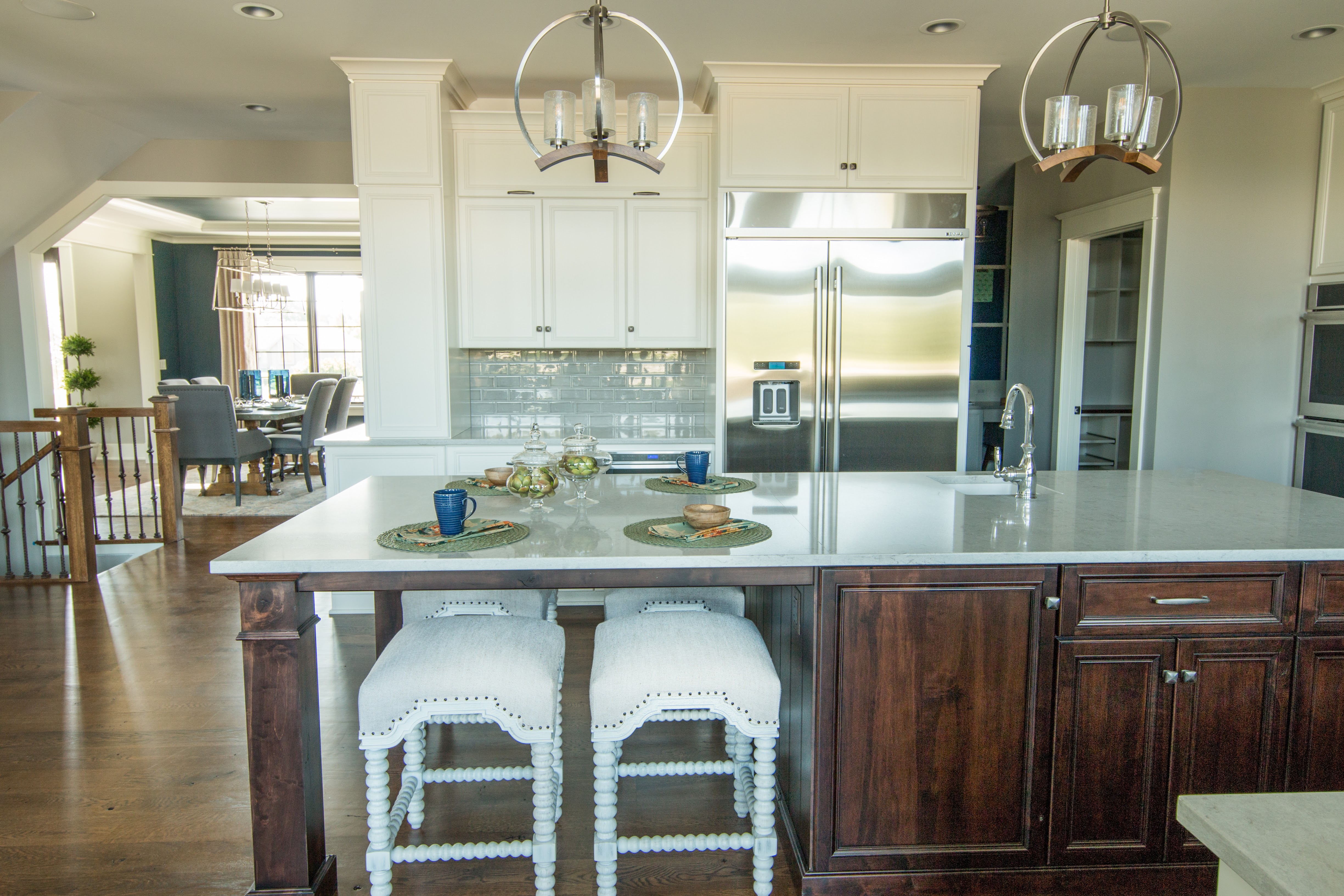 Dark kitchen island with white upholstered stools and farmhouse style pendant lighting