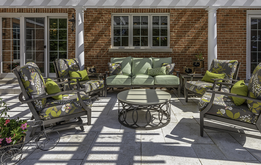Patio next to brick house with pergola and grey and green upholstered furniture