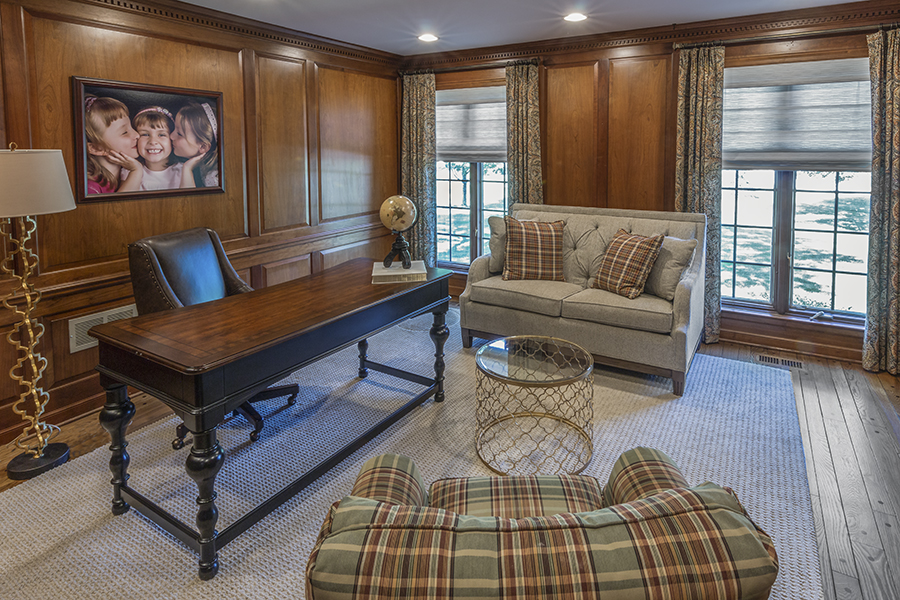Wood paneled home office with settee and plaid armchair
