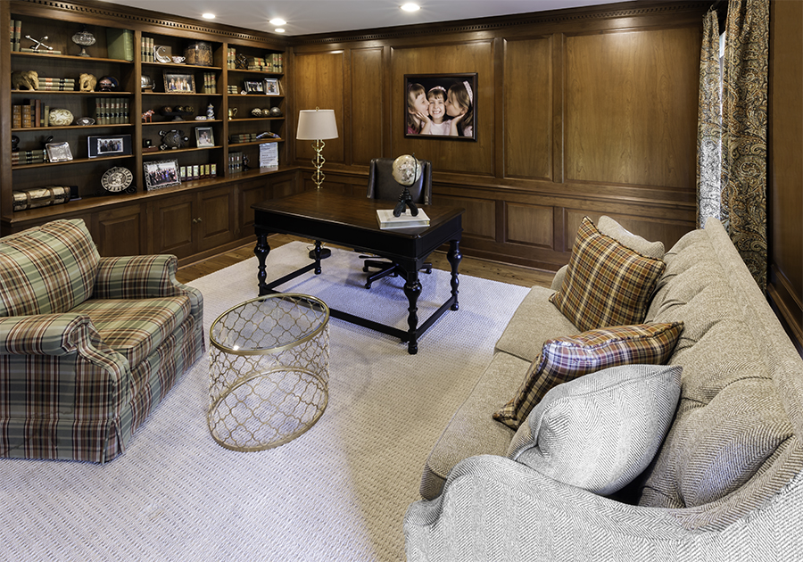 Wood paneled home office with built in book cases, plaid chair and small sofa