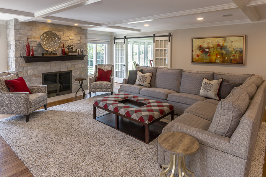 Grey and red palette family room with stone fireplace, sectional sofa, pair of armchairs and upholstered ottoman coffee table