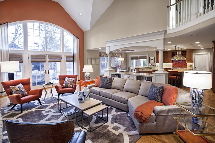 Two story family room with grey sofa, orange armchairs, blue accessories and orange accent wall