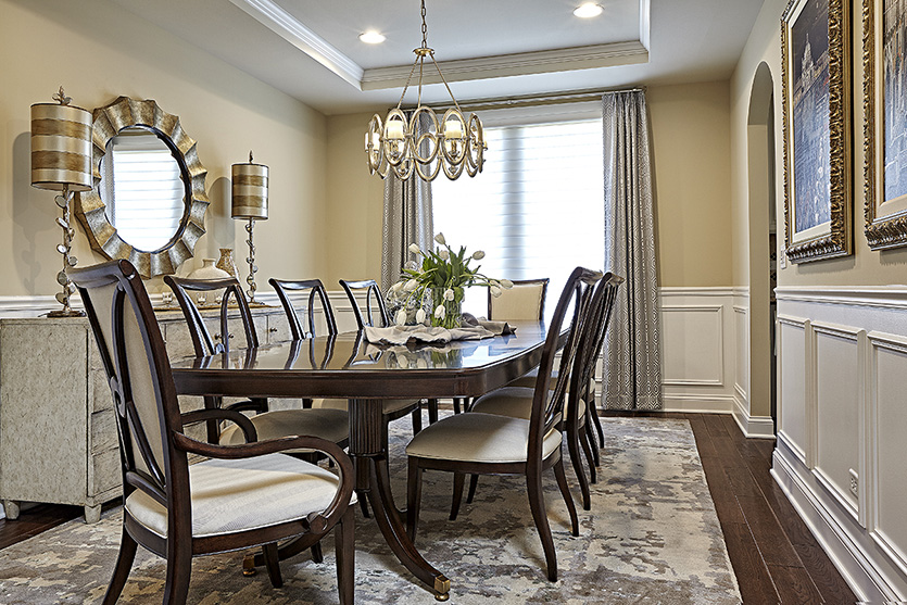 Dining room with dark wood and light upholstery, gold mirror and lighting and panel moulding