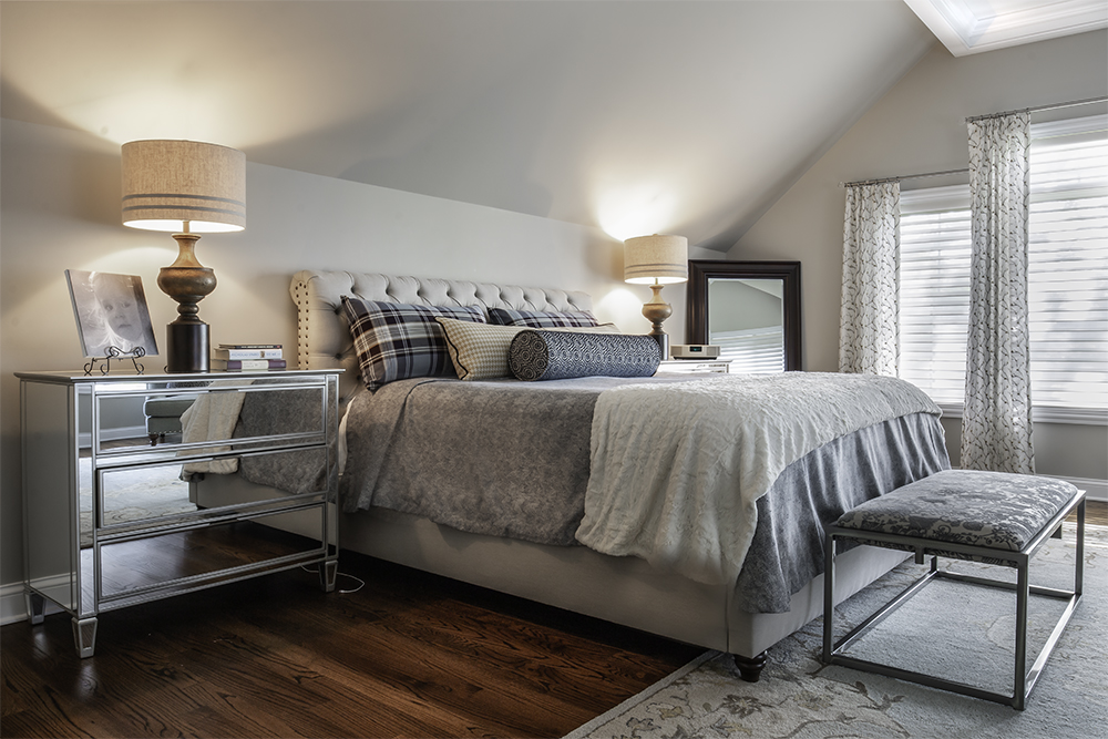 Main bedroom with mirrored nightstand, grey bedding, upholstered headboard and pair of lamps