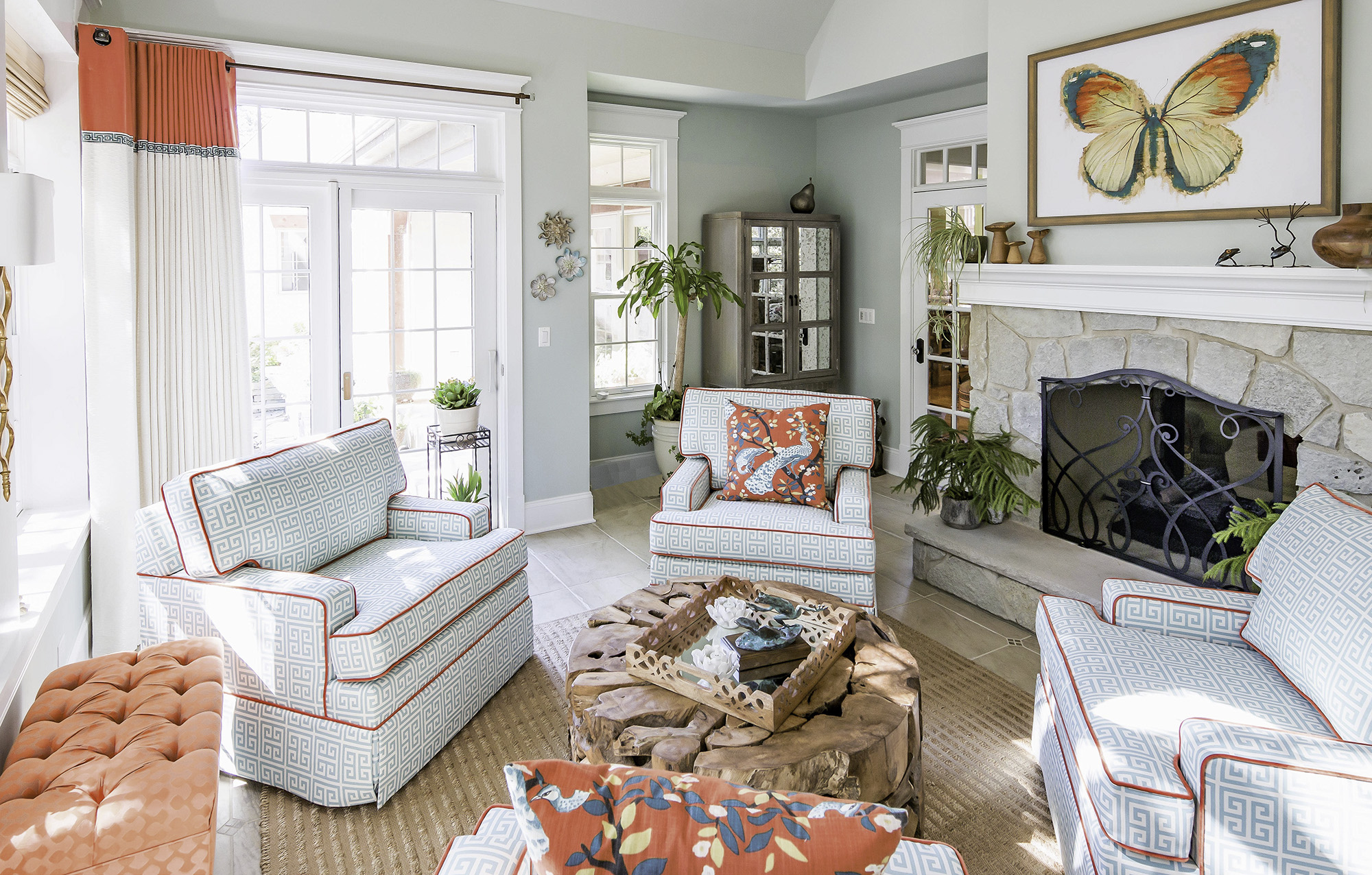 Sunroom with teal and coral upholstered furniture and butterfly artwork over the stone fireplace