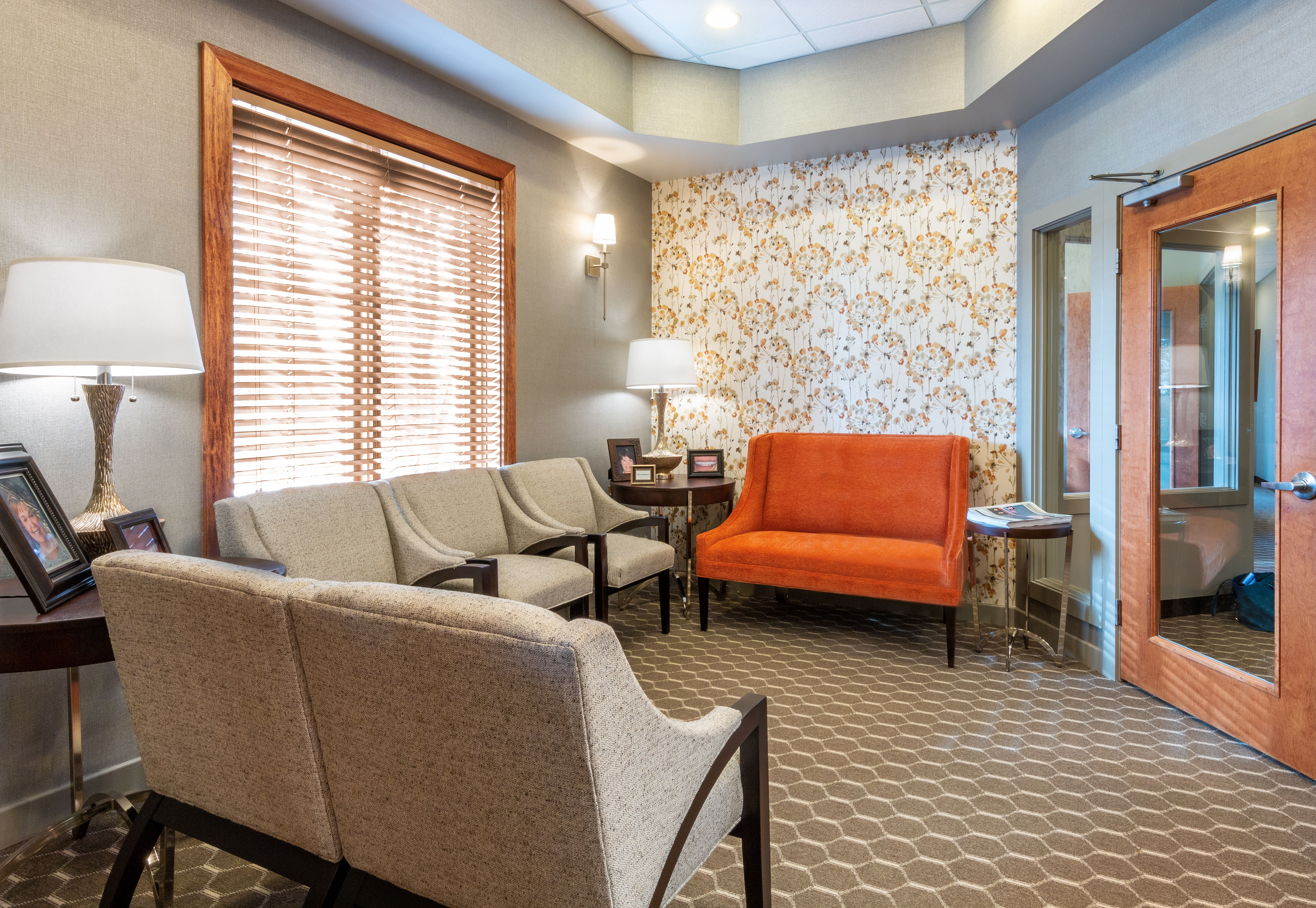 Waiting room with orange sofa in front of floral papered wall and 5 chairs