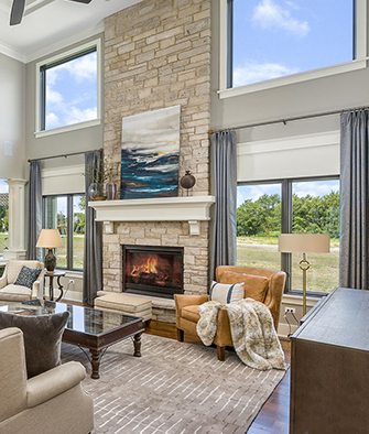 Model home with a stacked stone fireplace, leather chair, floor to ceiling windows and an open floor plan.