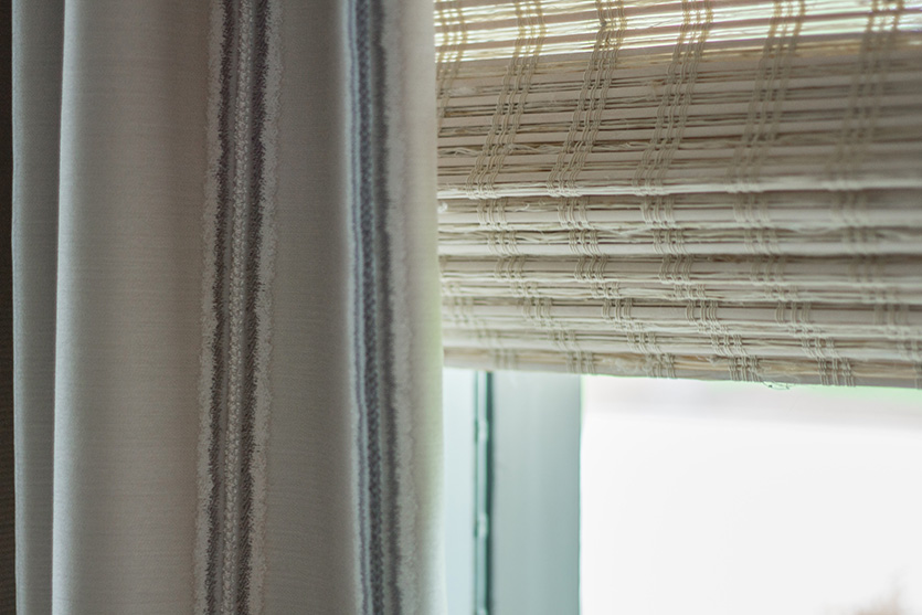 Light woven roman shade with grey drapery panel on window