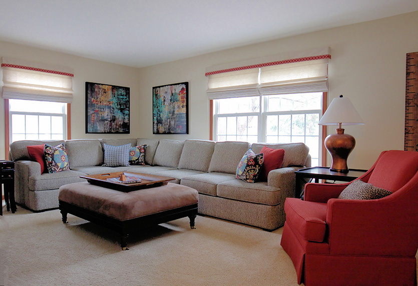 Living room with beige sectional, red chair, upholstered ottoman and modern artwork