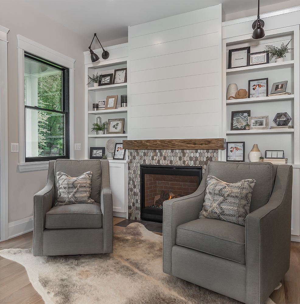 Grey swivel chairs in front of modern farmhouse fireplace and lighted bookshelves